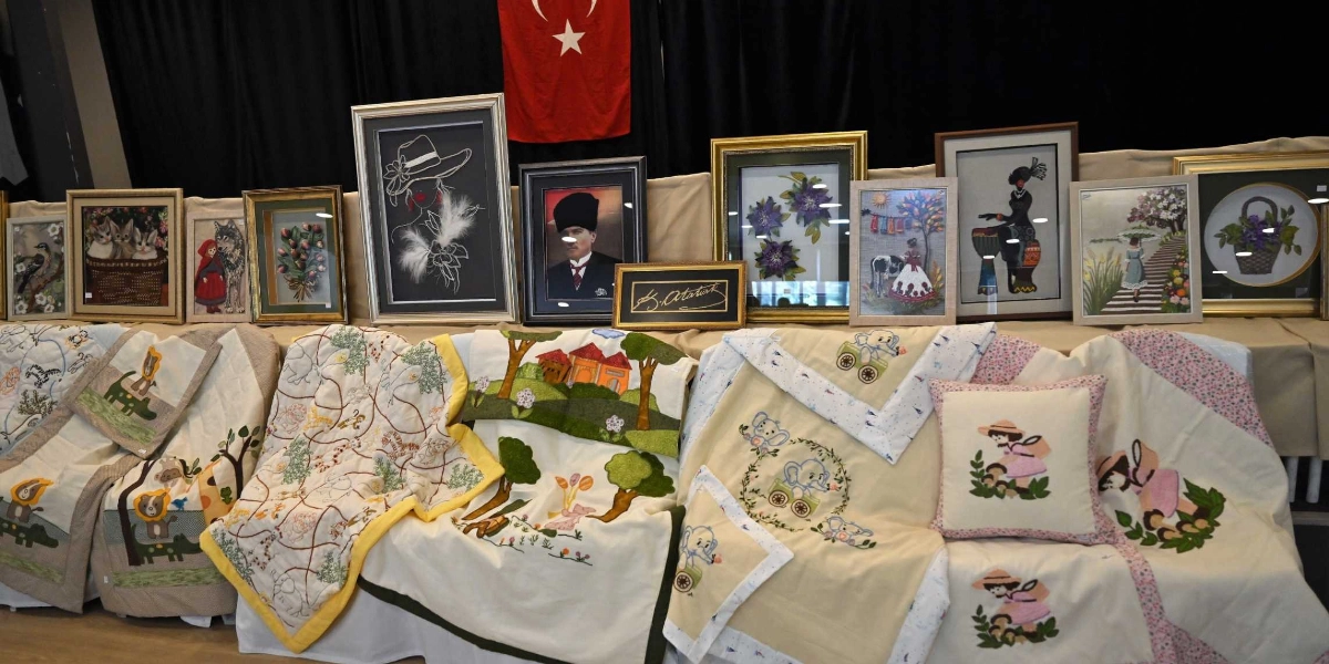 Atatürkçü Düşünce Derneği tarafından düzenlenen el emeği sergisinde, masanın üzerinde sergilenen çeşitli nakışlı örtüler, yastık kılıfları ve çerçevelenmiş el işi tablolar yer alıyor. Arka planda asılı Türk bayrağının önünde, Mustafa Kemal Atatürk'ün portresi, çiçek, hayvan ve insan figürlerinin işlendiği tablolar ile çocuk odası temalı nakışlı tekstil ürünleri sergileniyor.