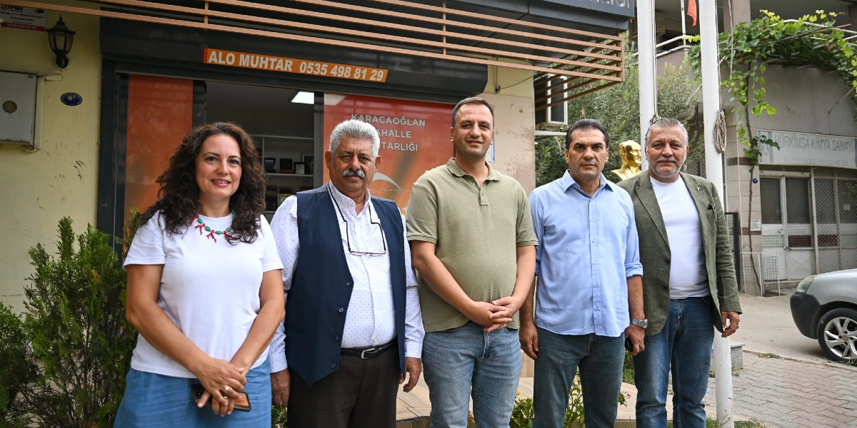 Karacaoğlan Mahalle Muhtarlığı binasının önünde yan yana duran, ikisi kadın üçü erkek olmak üzere beş kişilik bir grup. Arka planda üzerinde 