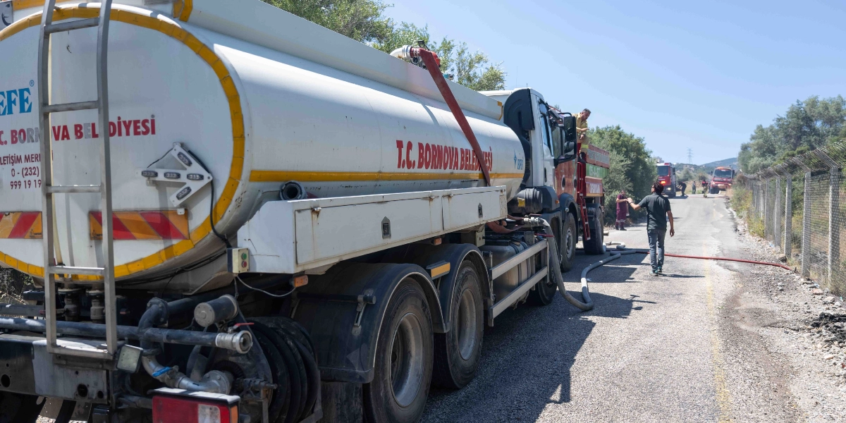 T.C. Bornova Belediyesi'ne ait beyaz bir su tankeri, yol kenarında park halinde duruyor. Tankerin üzerinde 