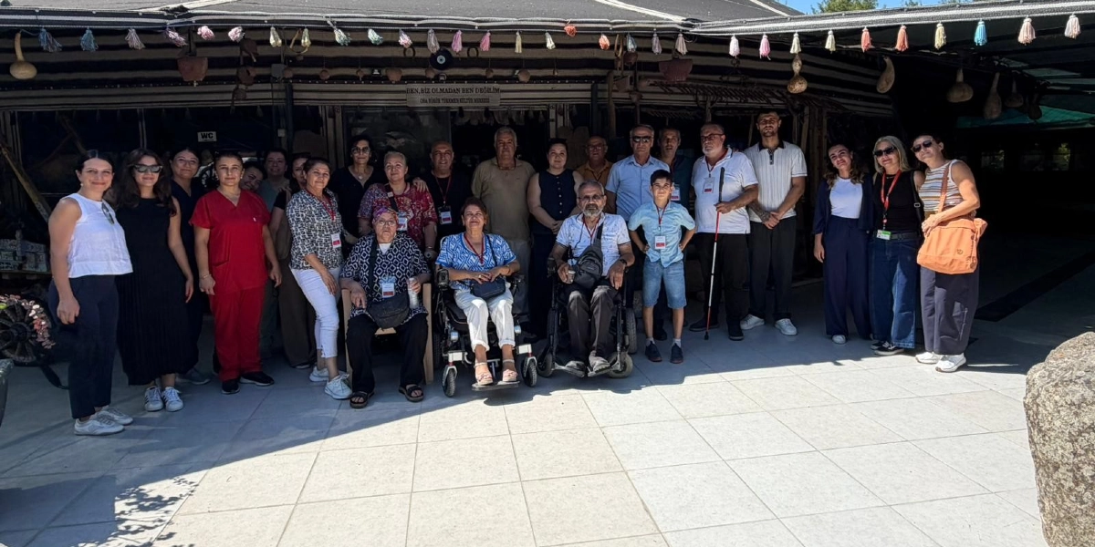 Geleneksel bir çadırın önünde, tekerlekli sandalyedeki bireyler, beyaz baston kullanan bir kişi ve çeşitli yaş gruplarından katılımcıların yer aldığı, engelli bireylere yönelik düzenlenen kültür gezisine katılan kalabalık bir grup.