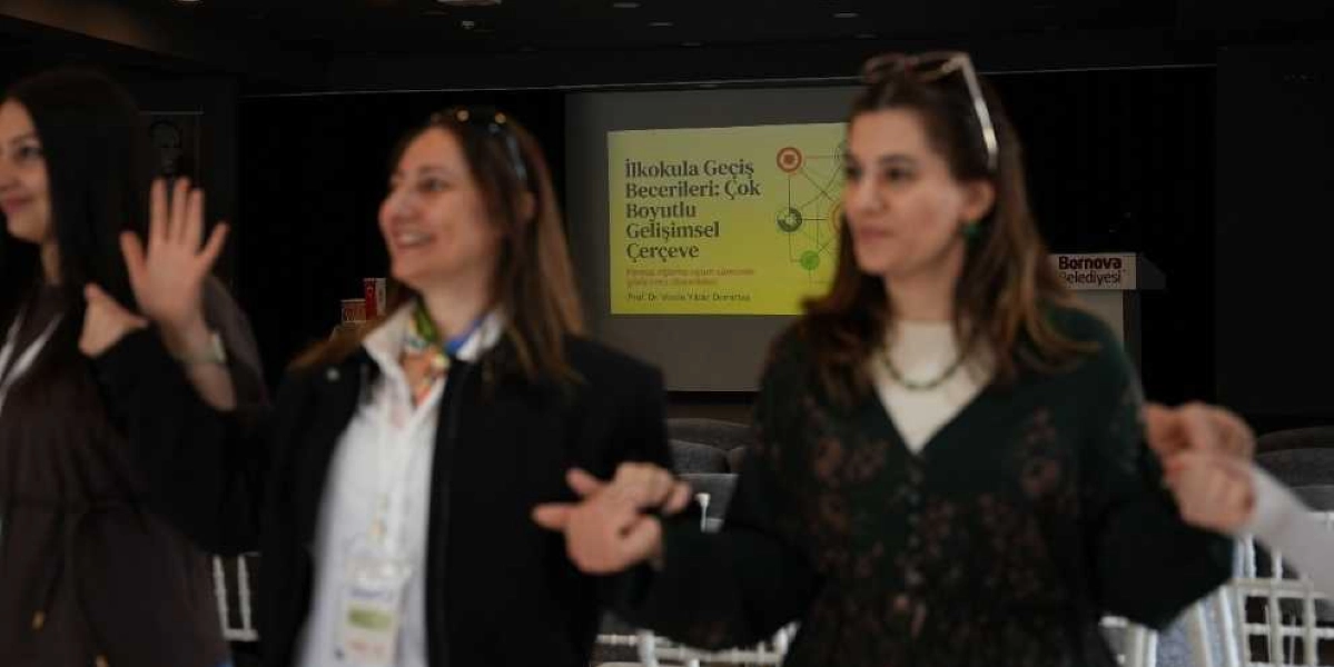 Bir konferans salonunda el ele tutuşarak gülümseyen üç kadın katılımcı, arka planda üzerinde 