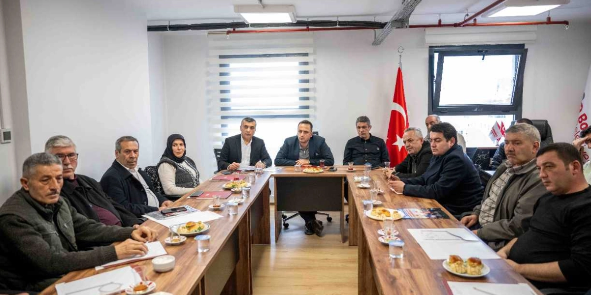 Başkan Ömer Eşki, U-şeklindeki bir toplantı masasında bir grup muhtarla bir araya gelerek görüşme yapıyor. Toplantı odasında arka planda Türk bayrağı yer alırken, masanın üzerinde not kağıtları, çay bardakları ve ikramlık tabaklar bulunuyor.