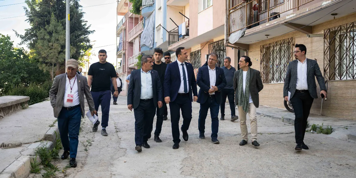 Bornova'da bir sokakta incelemelerde bulunan, aralarında Bornova Belediye Başkanı Ömer Eşki'nin de bulunduğu takım elbiseli ve günlük kıyafetli bir grup erkek, yokuşlu bir yolda yürüyerek çevreyi gözlemliyor.