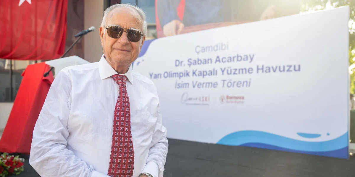 Beyaz gömlekli ve kırmızı desenli kravatlı, güneş gözlüğü takan Dr. Şaban Acarbay, arkasında 