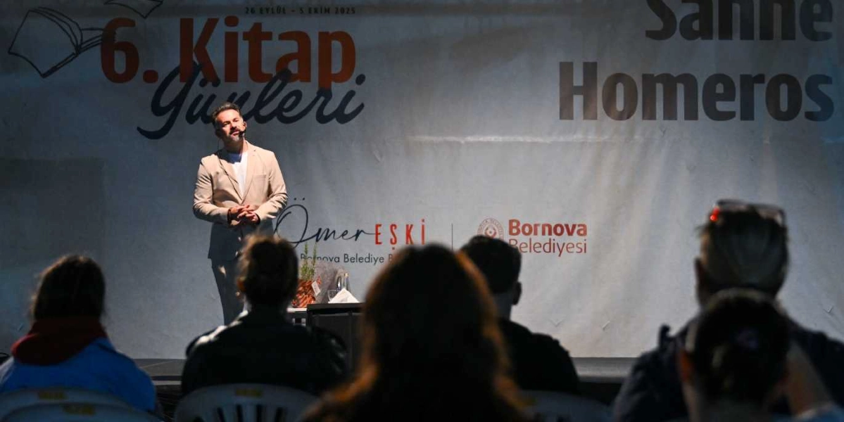 Bej renkli ceket giymiş bir konuşmacı, arkasında 6. Kitap Günleri ve Bornova Belediyesi logolarının bulunduğu bir sahnede dinleyicilere hitap ediyor. Sahne arkasındaki dev pankartta 26 Eylül - 5 Ekim tarihleri ve Ömer Eşki ismi yer alıyor. Ön planda ise sahneyi izleyen dinleyicilerin silüetleri görülüyor.