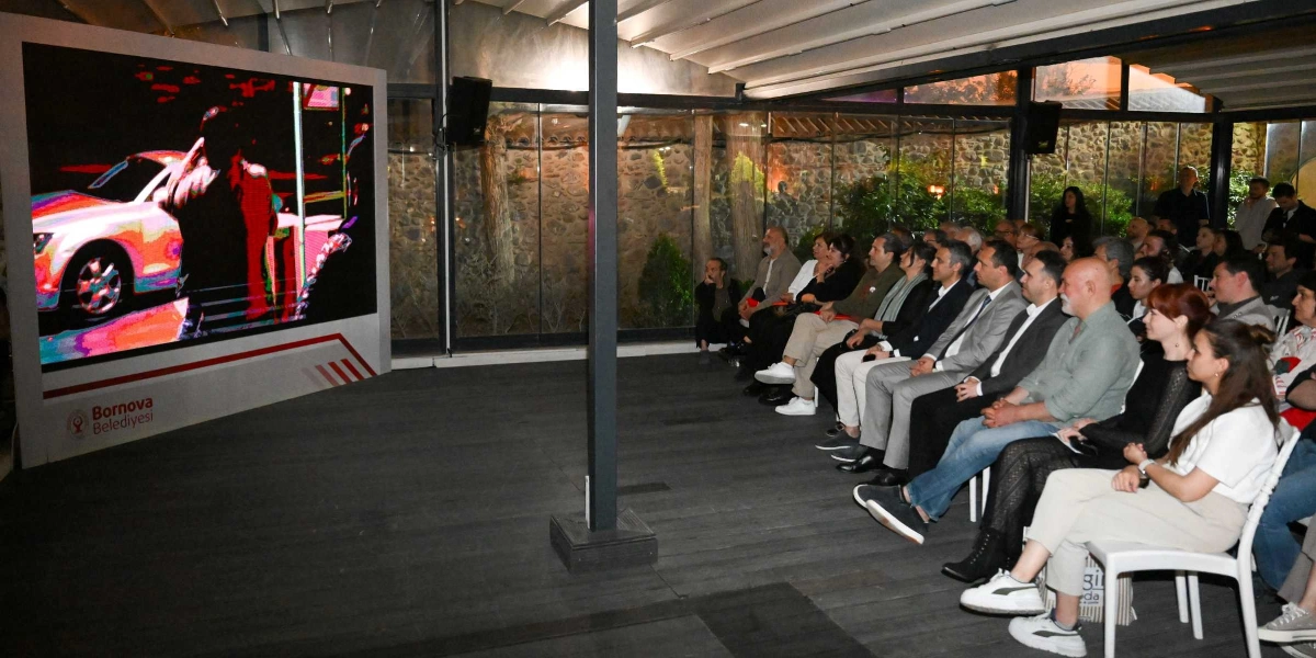 Bornova Belediyesi tarafından düzenlenen bir etkinlikte, kapalı bir alanda toplanan izleyiciler dev bir ekranda gösterilen sinema filmini izliyor. İzleyiciler yan yana dizilmiş sandalyelerde otururken, ekranın sol alt köşesinde Bornova Belediyesi logosu yer alıyor.