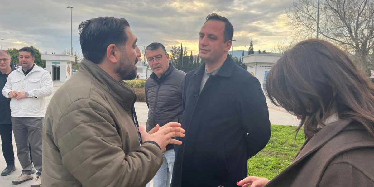 Dış mekanda, gün batımına yakın bir saatte bir araya gelmiş bir grup insan. Ön planda, haki renkli şişme montlu bir adam, yanındaki koyu renkli kaban giymiş bir adamla konuşurken elleriyle jest yapıyor. Arka planda ise gözlüklü, koyu renkli montlu bir adam ve daha geride beyaz ceketli başka bir kişi duruyor. Sağ tarafta ise sırtı dönük, kahverengi kabanlı bir kadın yer alıyor.