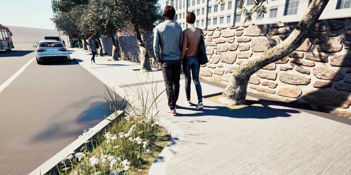 Modern bir şehir caddesinde, yan yana yürüyen bir çiftin arkadan görünümü. Kaldırımın bir tarafında doğal taş duvar ve ağaçlar, diğer tarafında ise beyaz çiçekli bitkilerle düzenlenmiş bir yeşil alan bulunuyor. Arka planda modern bir bina ve yolda ilerleyen bir otomobil yer alıyor.