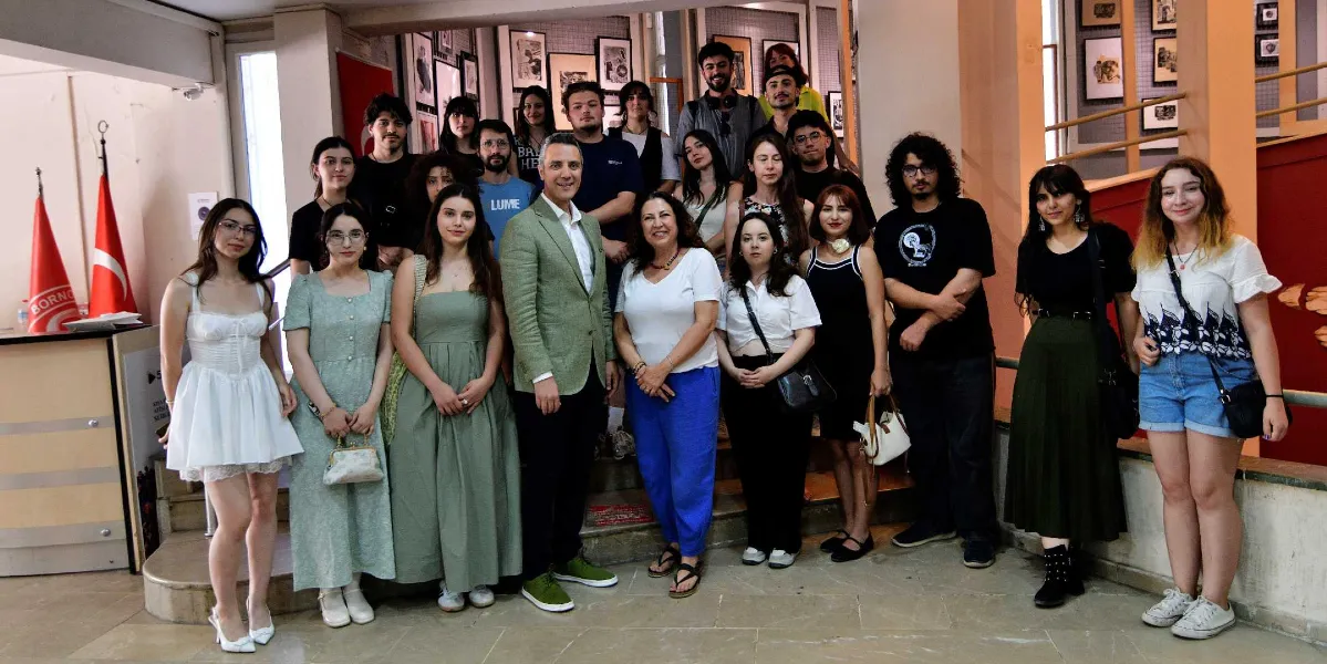 Bornova'da düzenlenen bir sergide, aralarında Bornova Belediye Başkanı'nın da bulunduğu kalabalık bir grup, sergi salonunun merdivenlerinde yan yana durarak objektiflere gülümsüyor. Arka planda duvarlarda çerçevelenmiş sanat eserlerinin asılı olduğu sergi alanı görülüyor.