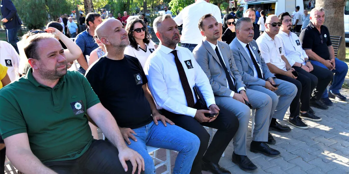 Açık havada düzenlenen bir anma töreninde yan yana sandalyelerde oturan bir grup insan. Katılımcıların birçoğu, Srebrenica soykırımını simgeleyen 