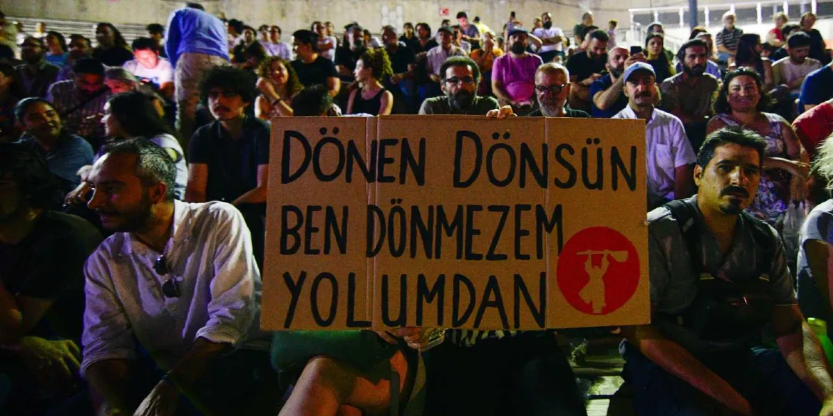 Açık havada düzenlenen bir anma etkinliğinde, kalabalık bir izleyici grubu arasında bir kişi, üzerinde 