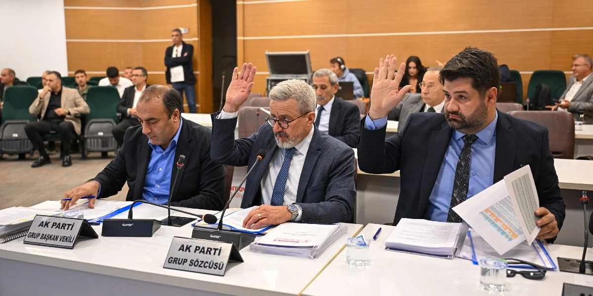 Bornova Belediyesi meclis toplantısında, önlerinde AK Parti Grup Başkan Vekili ve AK Parti Grup Sözcüsü yazılı isimlikler bulunan üç erkek üye, ellerini kaldırarak oylamaya katılıyor. Masada Bornova Belediyesi logolu dosyalar ve mikrofonlar yer alıyor.
