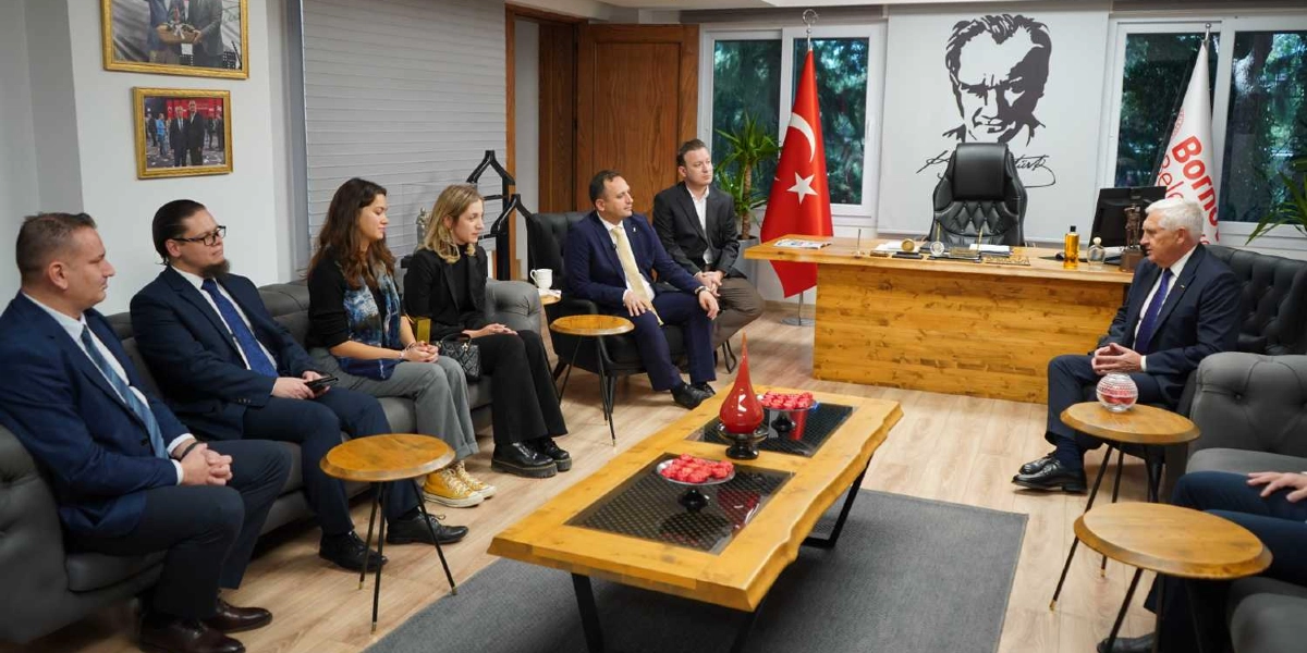 Bornova Belediye Başkanı'nın makam odasında gerçekleşen resmi bir görüşmede, Bornova Belediyesi yetkilileri ve Białystok'tan gelen heyet üyeleri karşılıklı koltuklarda oturuyor. Odanın arka planında Türk bayrağı, Atatürk portresi ve Bornova Belediyesi'nin flaması yer alıyor. Ortada ahşap bir sehpa ve üzerinde ikramlıklar bulunuyor. Katılımcılar resmi kıyafetler içinde, samimi bir atmosferde sohbet ediyor.