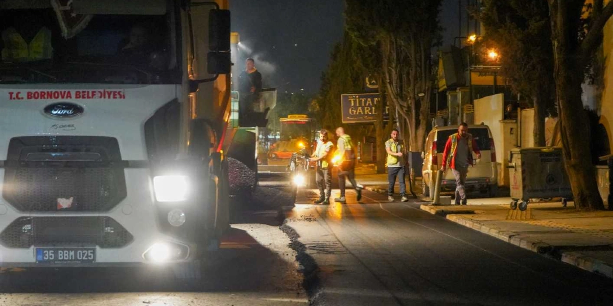 Gece saatlerinde bir cadde üzerinde asfalt yenileme çalışması yapan Bornova Belediyesi ekipleri. Ön planda üzerinde T.C. Bornova Belediyesi yazılı beyaz bir Ford kamyon, arka planda ise iş makineleri ve reflektörlü yelek giymiş belediye çalışanları görülüyor.