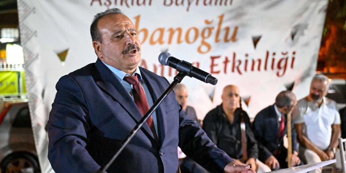 Koyu renk takım elbiseli, bıyıklı bir adam, arkasında 