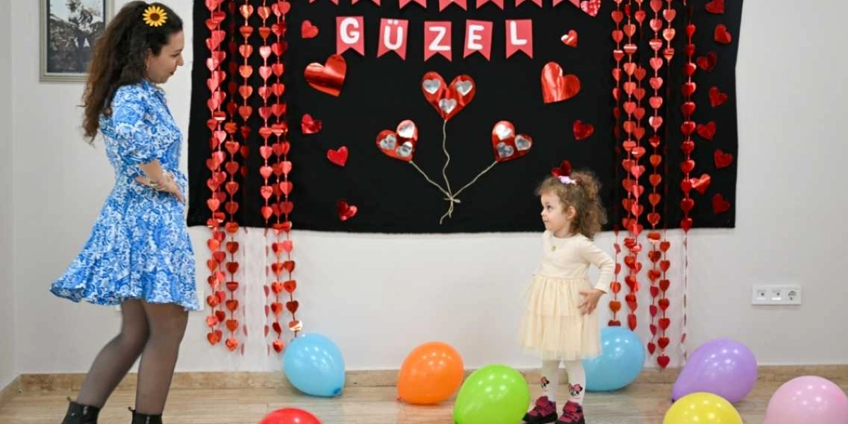 Mavi beyaz desenli elbiseli bir kadın ile krem rengi tüllü elbise giyen küçük bir kız çocuğu, üzerinde kırmızı kalp süslemeleri ve 