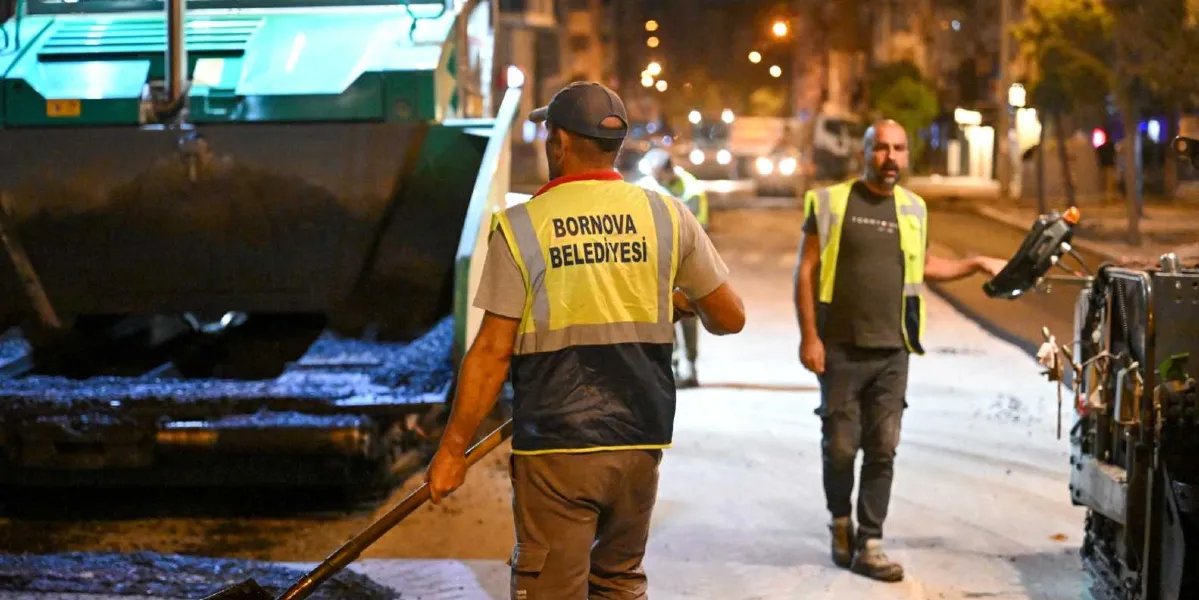 Gece vakti Mustafa Kemal Caddesi'nde asfalt serme çalışması yapan Bornova Belediyesi personeli. Ön planda sırtı dönük, üzerinde 