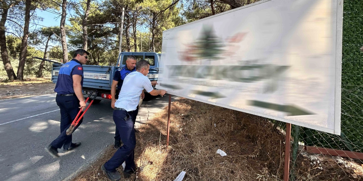 Bornova Belediyesi zabıta ekipleri, yol kenarındaki büyük bir reklam tabelasını sökmek için çalışma yapıyor. Üniformalı zabıta memurlarından biri elinde büyük bir kesici alet tutarken, diğer iki memur tabelayı yerinden çıkarmaya çalışıyor. Arka planda ise üzerinde Bornova Belediyesi logosu bulunan mavi bir kamyonet park halinde bekliyor.