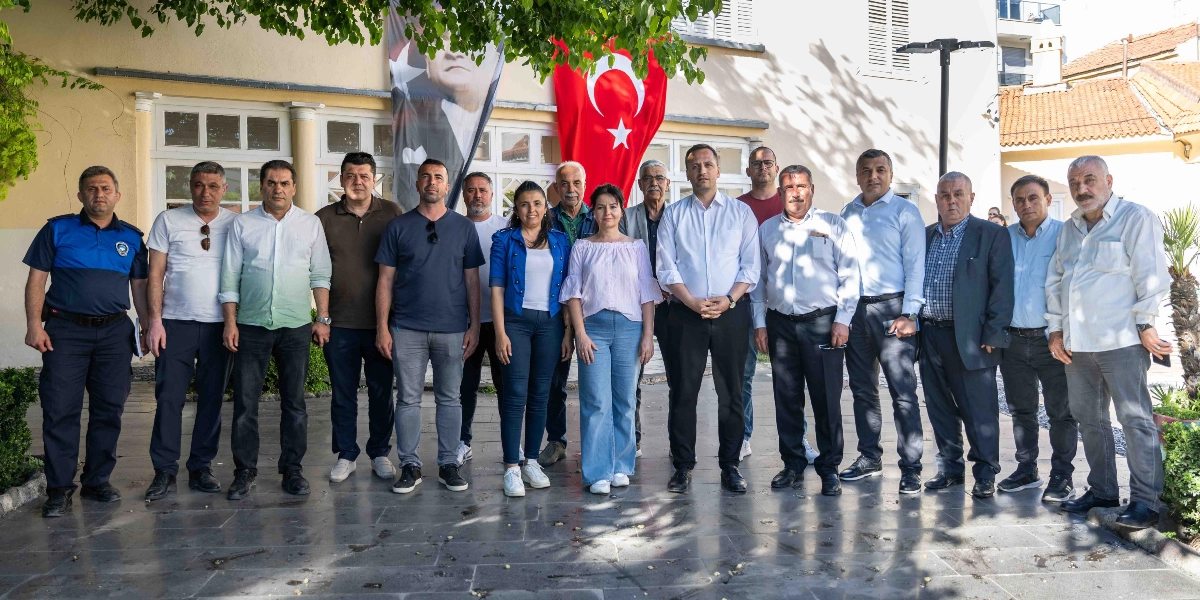 Açık havada, arkalarında Türk bayrağı ve Atatürk posteri asılı olan tarihi bir binanın önünde yan yana duran, aralarında Bornova Belediye Başkanı Mustafa İduğ'un da bulunduğu kalabalık bir grup muhtar ve yerel yönetici. Çoğunluğu erkeklerden oluşan grup, günlük ve resmi kıyafetlerle objektife gülümseyerek poz veriyor.
