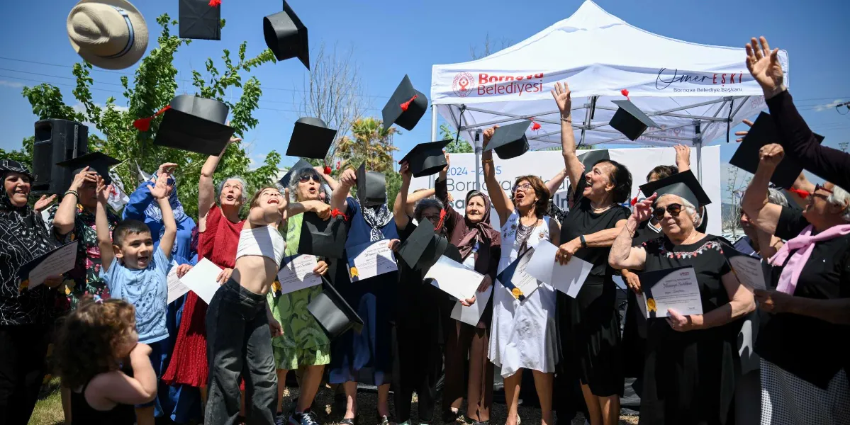 Açık havada, Bornova Belediyesi logolu beyaz bir çadırın önünde toplanan farklı yaş gruplarından kadınlar ve bir çocuk, ellerindeki mezuniyet keplerini neşeyle havaya atıyor. Birçoğunun elinde başarı belgeleri bulunan katılımcılar, güneşli bir günde düzenlenen mezuniyet töreninde sevinçlerini paylaşıyor.