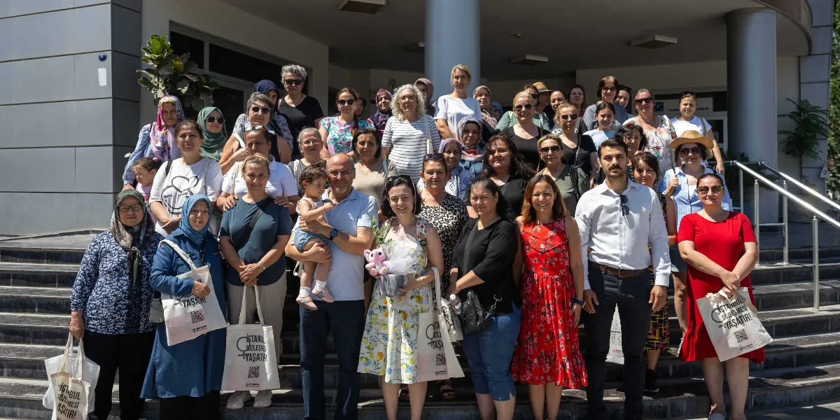 Bornova'da bir kamu binasının merdivenlerinde toplanmış, çoğunluğu kadınlardan oluşan kalabalık bir grup. Katılımcıların birçoğu ellerinde üzerinde 