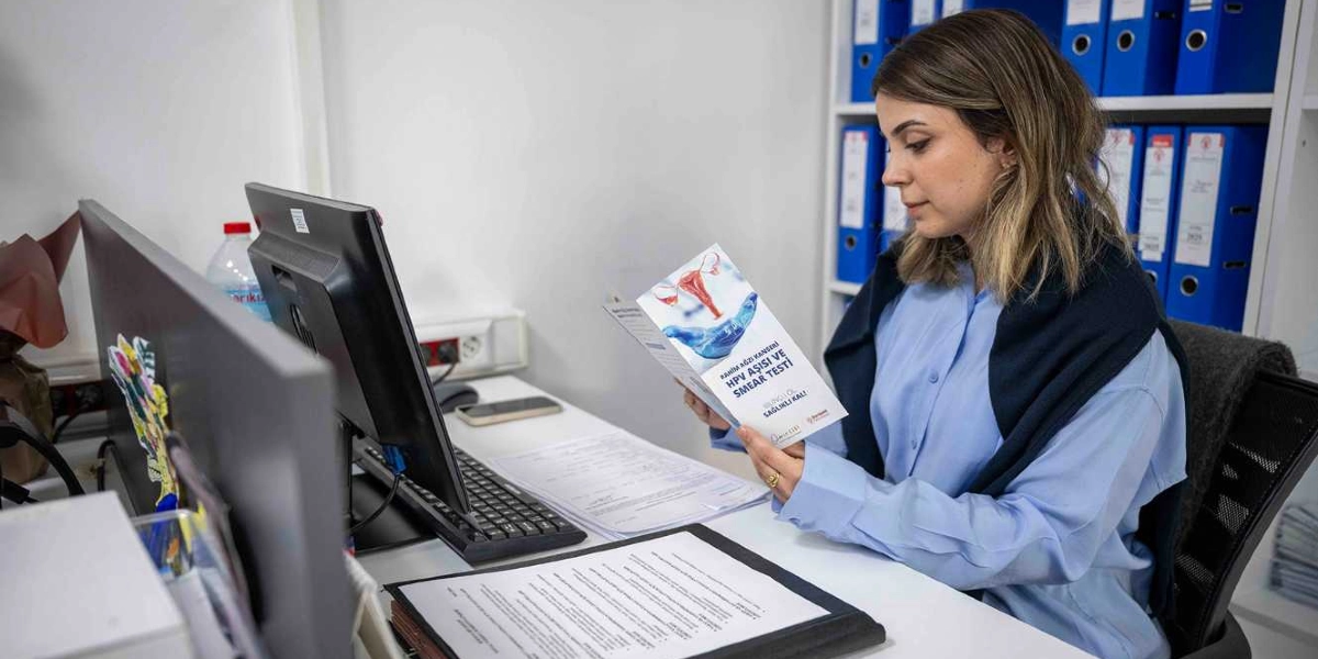 Ofis ortamında masasında oturan genç bir kadın, elinde tuttuğu 