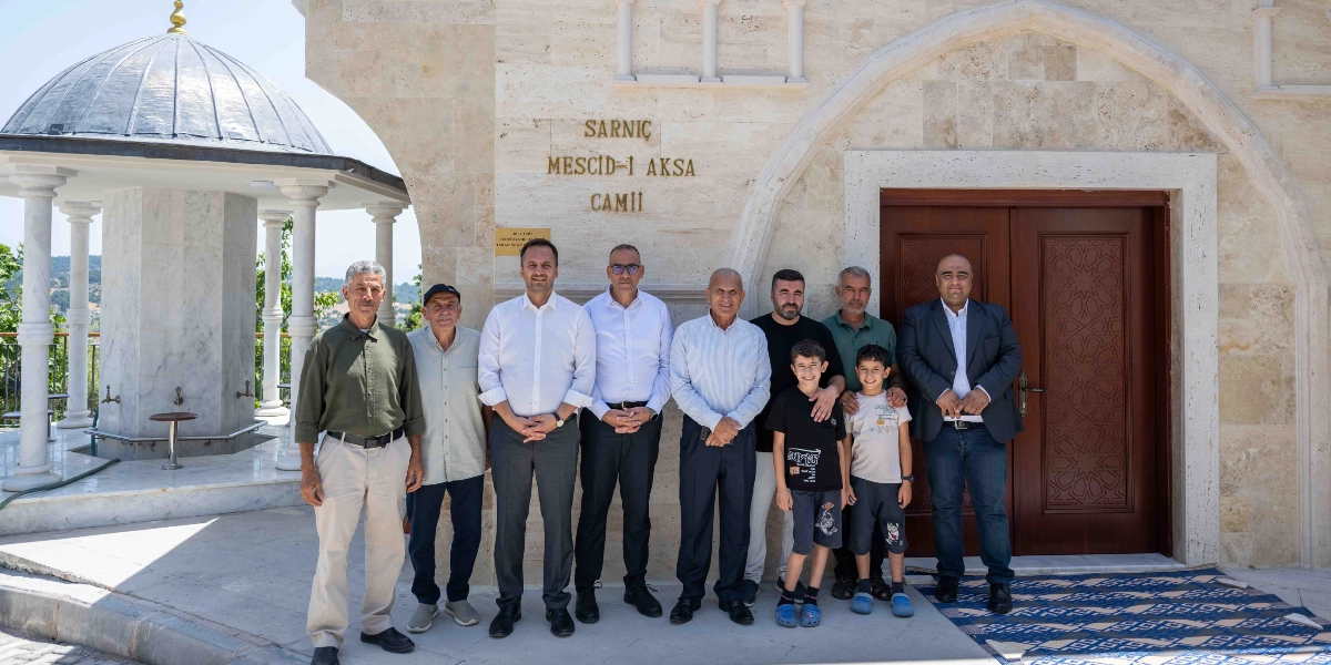 Sarnıç Mescid-i Aksa Camii'nin önünde yan yana duran, aralarında iki çocuğun da bulunduğu bir grup erkek. Taş duvarlı cami girişinin üzerinde 