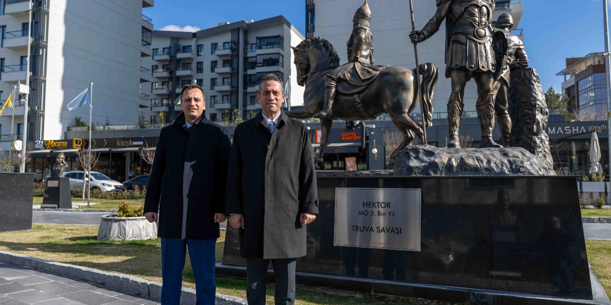 Ali Mahir Başarır ve yanında bulunan bir kişi, Bornova'da Hektor ve Truva Savaşı'nı temsil eden bronz bir heykelin önünde yan yana durarak kameraya gülümsüyor. Heykelin kaidesinde 