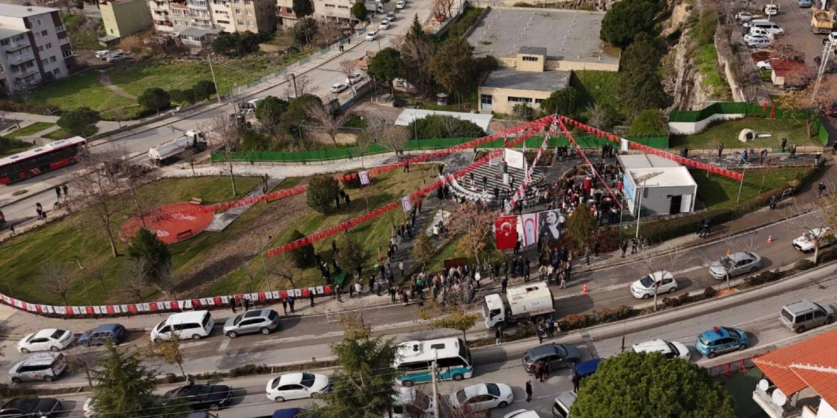 Bornova'da düzenlenen anma töreninde, Rauf Denktaş'ın anıtının bulunduğu park alanı Türk ve Kuzey Kıbrıs Türk Cumhuriyeti bayraklarıyla süslenmiş. Havadan çekilen görüntüde, anıt çevresinde toplanan kalabalık, tören alanı, çevredeki yollar ve yoğun trafik akışı görülüyor.