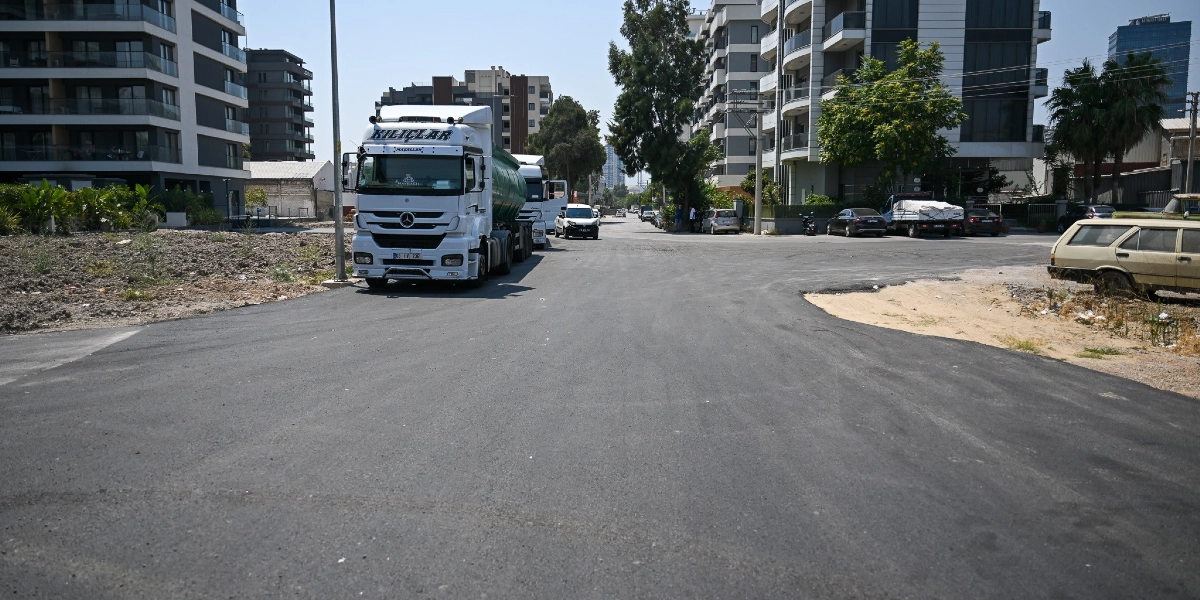 Yeni asfaltlanmış geniş bir yolun kenarında park halinde duran Kılıçlar logolu beyaz bir tır ve çevresinde modern çok katlı konut binalarının bulunduğu bir şehir sokağı görünümü.