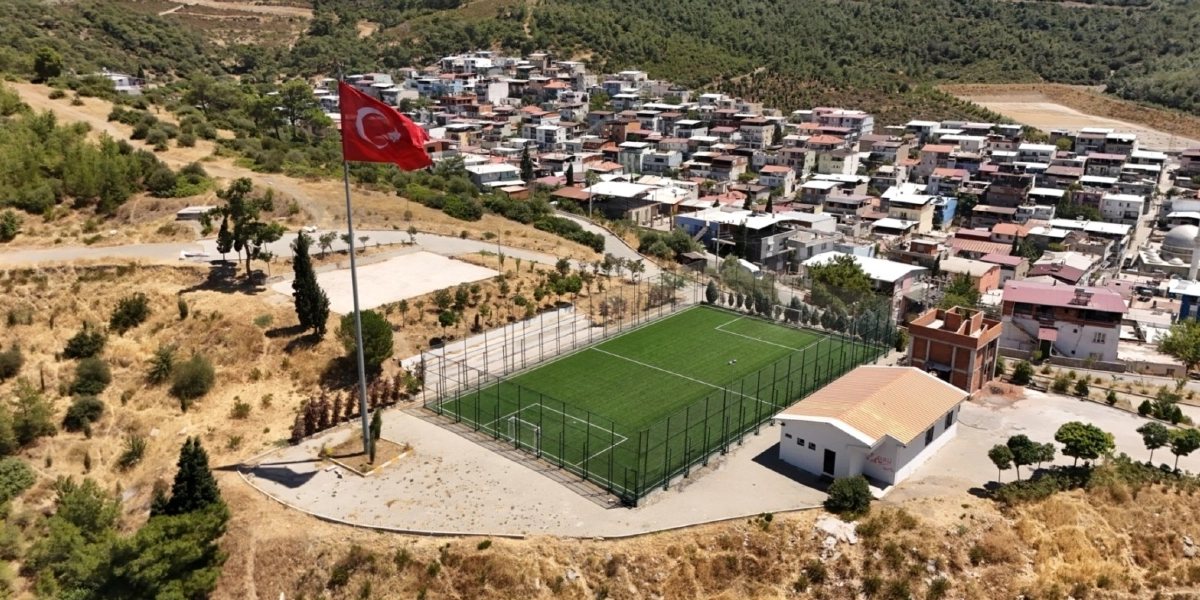 Bornova'da yamaç üzerine kurulu yerleşim yerinin hemen yanında, etrafı tellerle çevrili suni çim halı saha, yanında tek katlı bir yapı ve yüksek bir direkte dalgalanan Türk bayrağı görülüyor.