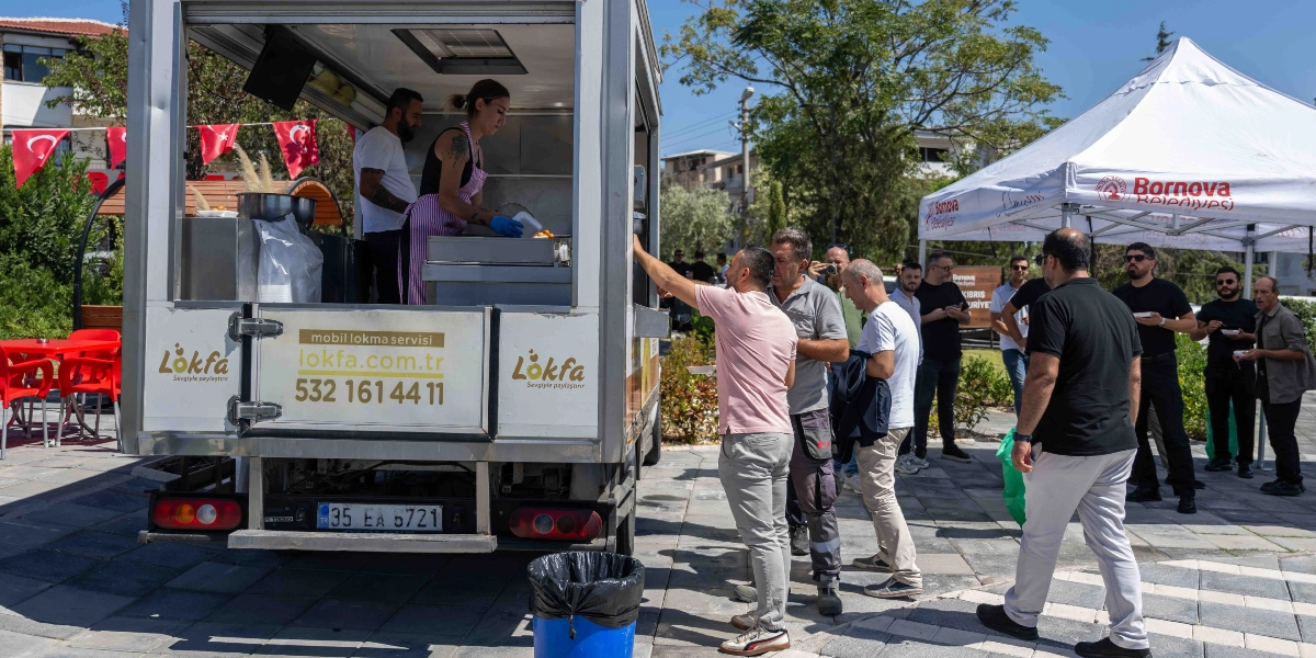 Açık havada kurulan bir mobil lokma servisi aracından vatandaşlara lokma dağıtılıyor. Aracın üzerinde 