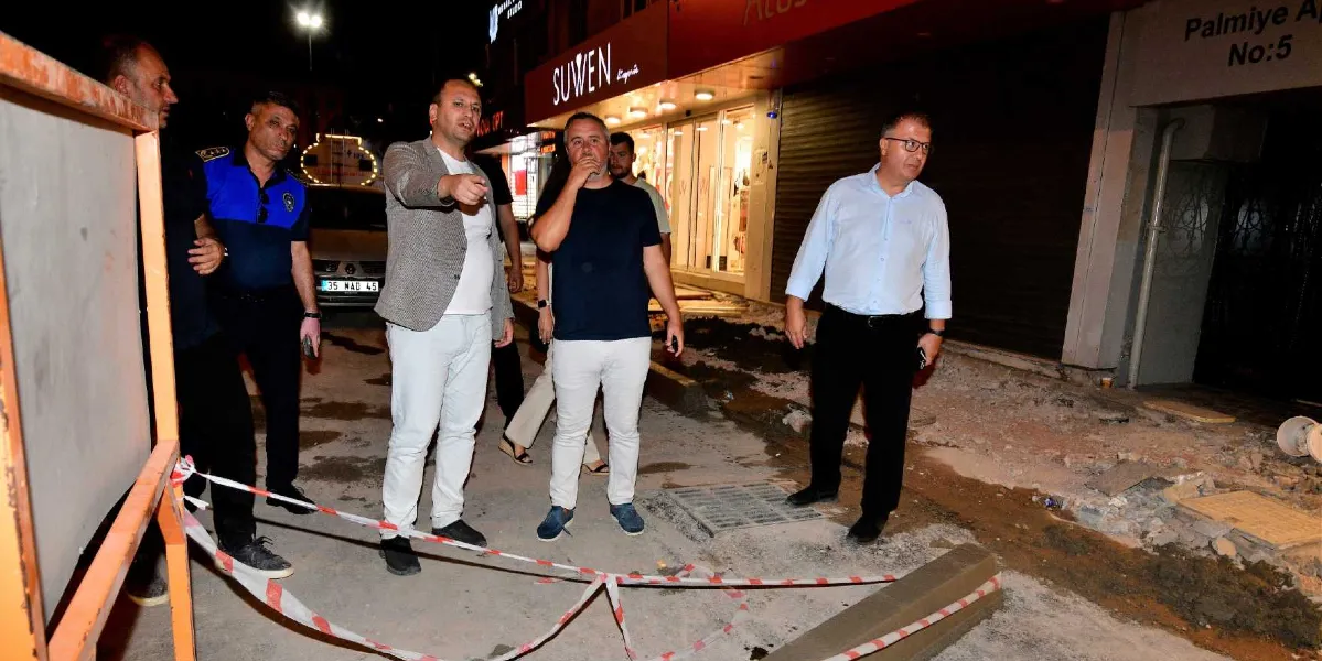 Gece vakti Bornova'da bir cadde üzerinde incelemelerde bulunan bir grup yetkili. Önde gri ceketli bir kişi eliyle yolu işaret ederken, yanında lacivert tişörtlü bir kişi ve açık mavi gömlekli bir beyefendi yer alıyor. Grubun arkasında bir polis memuru ve diğer görevliler bulunuyor. Çalışma alanı kırmızı beyaz şeritlerle çevrilmiş durumda, arka planda ise Suwen mağazası ve Palmiye Apartmanı tabelası görülüyor.