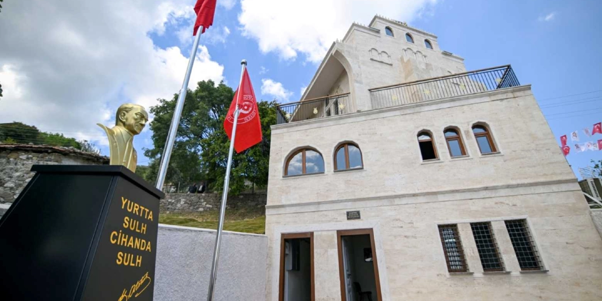 Açık renkli taş kaplamalı, kemerli pencerelere sahip üç katlı bir bina ve önünde üzerinde 