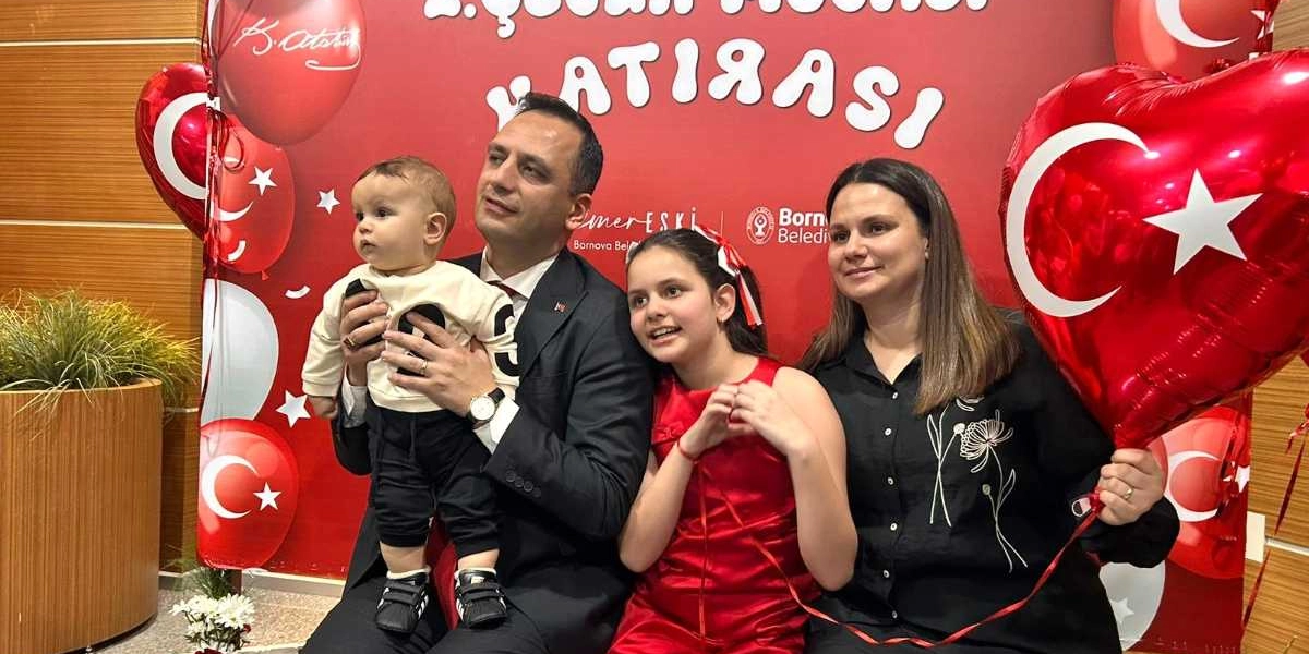 Bornova Belediyesi tarafından hazırlanan 23 Nisan temalı kırmızı bir fon önünde poz veren dört kişilik bir aile. Takım elbiseli bir baba kucağında bebekle, yanında kırmızı elbiseli bir kız çocuğu ve siyah gömlekli bir kadın yer alıyor. Kadın elinde kalp şeklinde Türk bayraklı bir balon tutuyor. Arka planda 