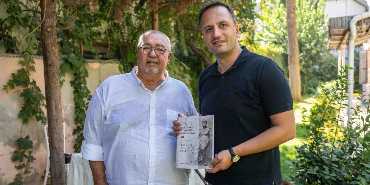 Yeşil bir bahçede yan yana duran iki erkekten sağdaki, üzerinde 