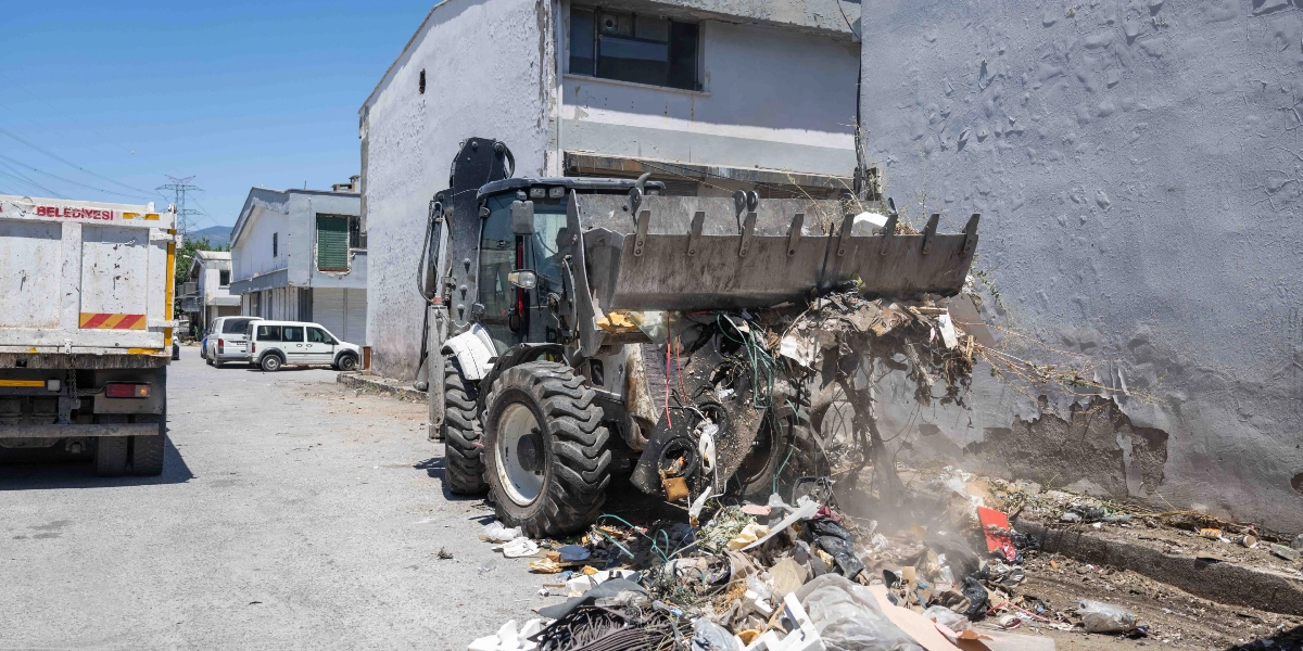 Bornova Belediyesi’ne ait bir iş makinesi, sokak kenarındaki ayakkabı atıkları ve çeşitli çöpleri kepçesiyle toplayarak kamyona yüklemek üzere hazırlıyor.