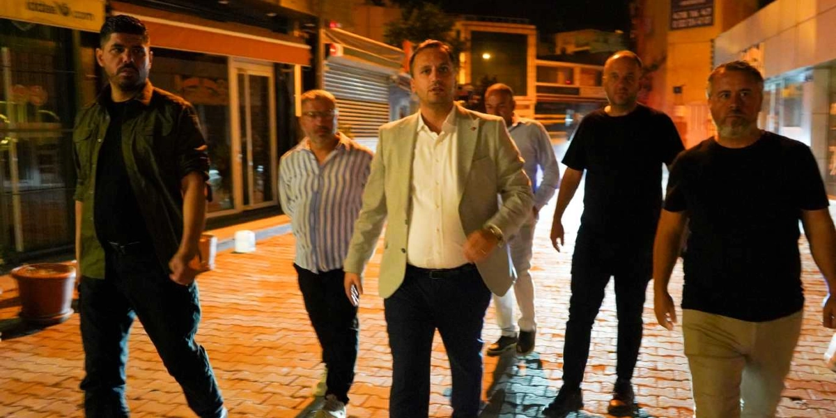 Gece vakti, kilit taşı döşeli bir sokakta yürüyen beş kişilik erkek grubu. Grubun önünde, açık renkli bir ceket ve beyaz gömlek giymiş bir kişi yer alıyor; arkasında ise günlük kıyafetler içindeki diğer dört kişi ona eşlik ediyor. Arka planda dükkan vitrinleri ve sokak aydınlatmaları görülüyor.
