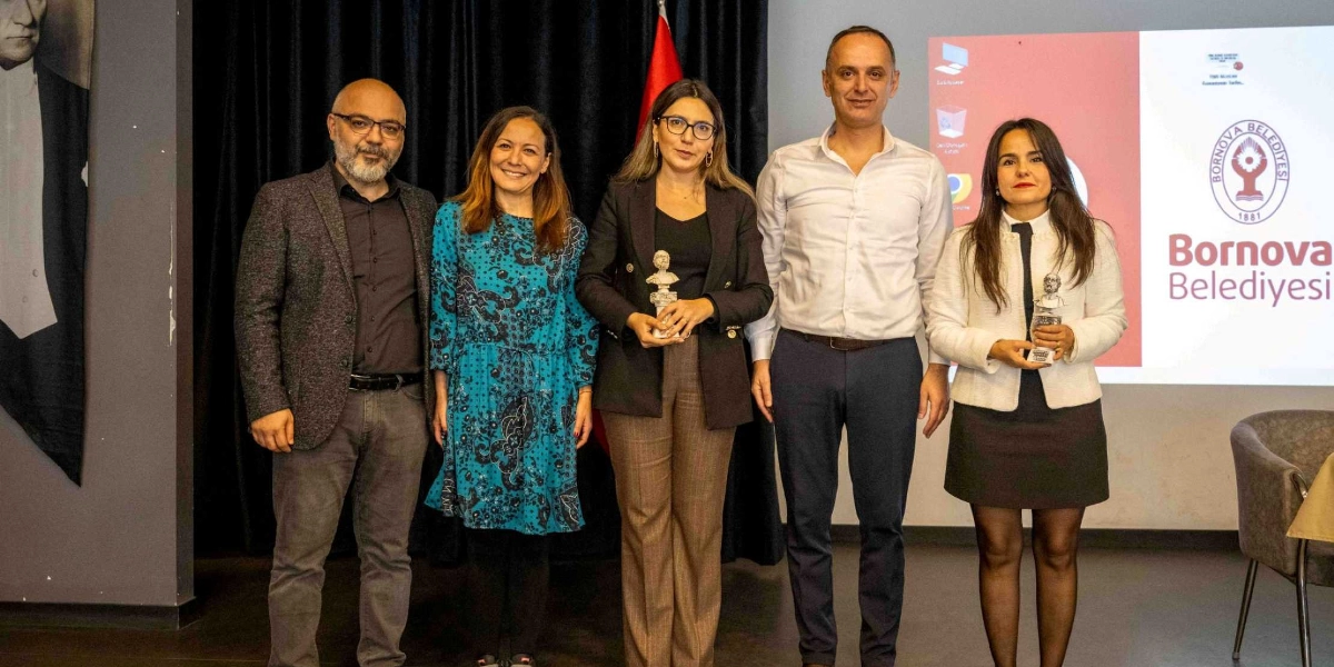 İç mekan bir etkinlikte yan yana duran üçü erkek, ikisi kadın toplam beş kişi objektiflere gülümsüyor. Ortadaki kadın ve en sağdaki kadın ellerinde küçük birer Atatürk büstü tutuyor. Arka planda Bornova Belediyesi logosunun ve isminin yer aldığı bir projeksiyon ekranı ile siyah bir perde bulunuyor. Sol tarafta ise Mustafa Kemal Atatürk'ün bir portresinin bir kısmı görünüyor.
