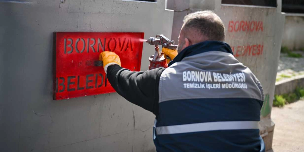 Bornova Belediyesi Temizlik İşleri Müdürlüğü üniforması giyen bir görevli, gri renkli yeni bir çöp konteynerinin üzerine sprey boya ile kırmızı renkte 