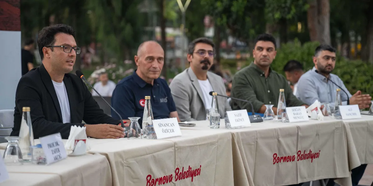 Açık havada düzenlenen bir panelde, Bornova Belediyesi yazılı örtülerle kaplı masada yan yana oturan beş konuşmacı yer alıyor. En solda konuşma yapan Prof. Dr. Zafer Akçığ bulunurken, yanında sırasıyla Sinancan Öziçer, Nazif Ekinci, Doğan Baran Mengüç ve Ali Kançmiş oturuyor. Her birinin önünde isimlerinin yazılı olduğu kartlar, mikrofonlar ve su şişeleri bulunuyor.