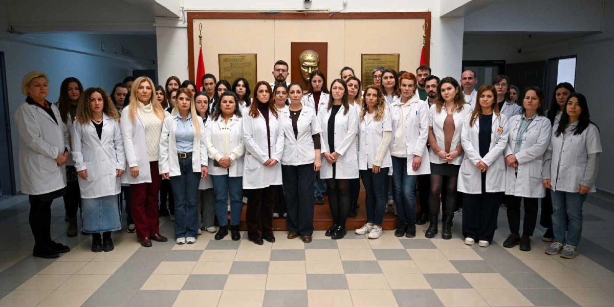Beyaz önlük giymiş kalabalık bir öğretmen grubu, arka planda Atatürk rölyefinin bulunduğu bir binanın giriş holünde yan yana durarak şiddete karşı tepkilerini göstermek amacıyla bir araya gelmiş.