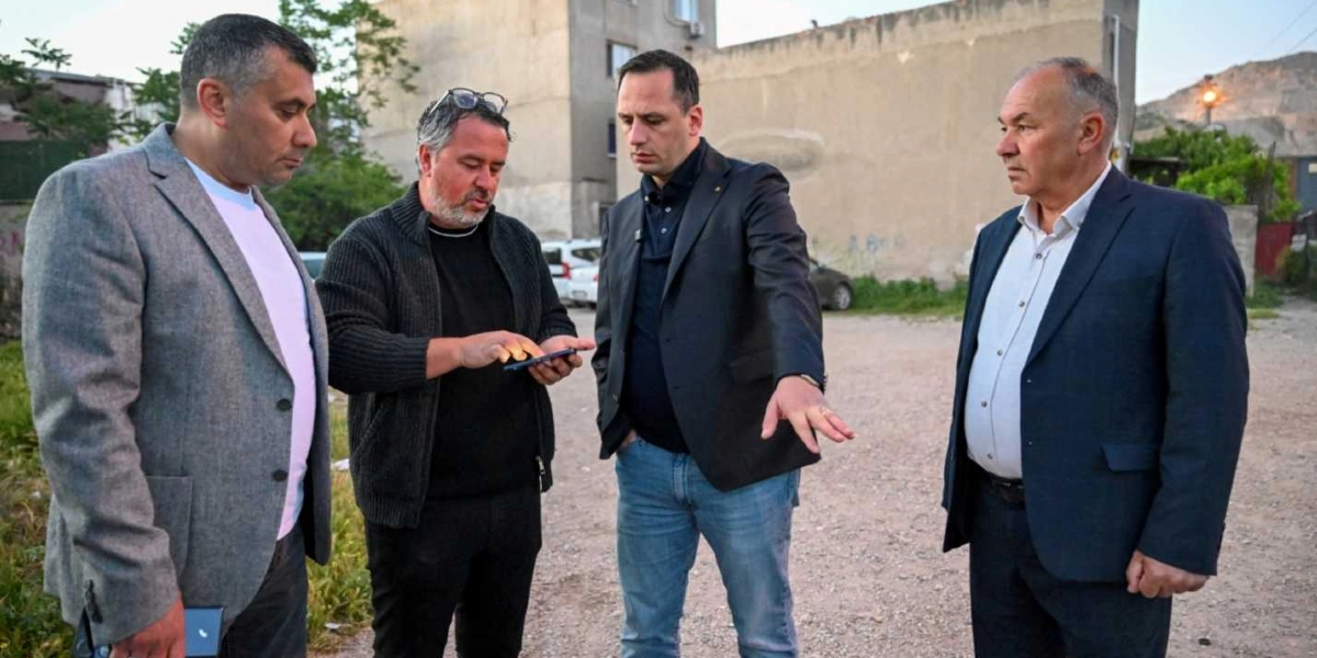 Egemenlik Mahallesi'nde açık bir alanda duran dört erkek, bir konu üzerinde inceleme yapıyor. Ortadaki iki kişiden biri elindeki telefona bakarken, diğeri eliyle çevredeki bir noktayı işaret ederek açıklama yapıyor. Yanlarındaki diğer iki kişi ise onları dikkatle dinliyor. Arka planda toprak bir zemin ve eski bir bina yapısı görülüyor.