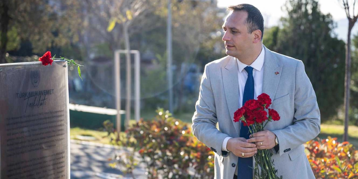 Açık renkli takım elbiseli ve lacivert kravatlı bir erkek, elinde tuttuğu bir demet kırmızı karanfili, üzerinde 
