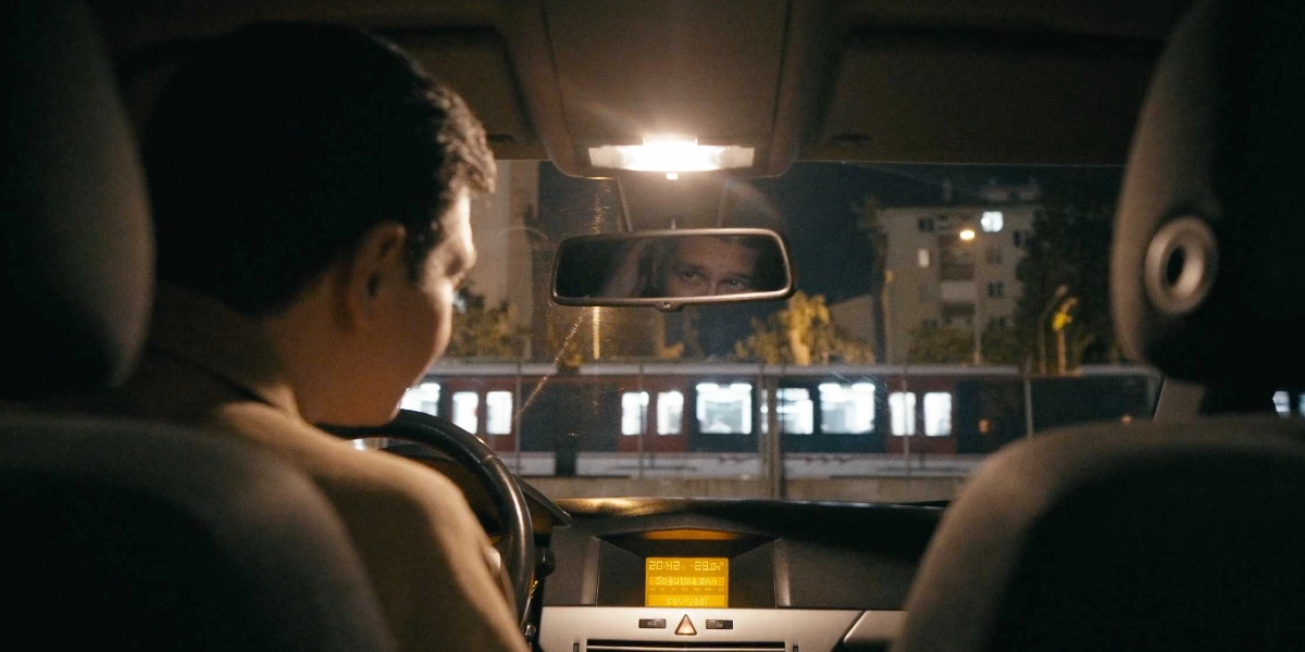 Gece vakti bir otomobilin sürücü koltuğunda oturan genç bir adam, direksiyon başında ön tarafa bakıyor. Dikiz aynasında adamın gözleri ve yüzünün bir kısmı yansıyor. Otomobilin ön panelindeki dijital ekranda saat 20:42 ve 