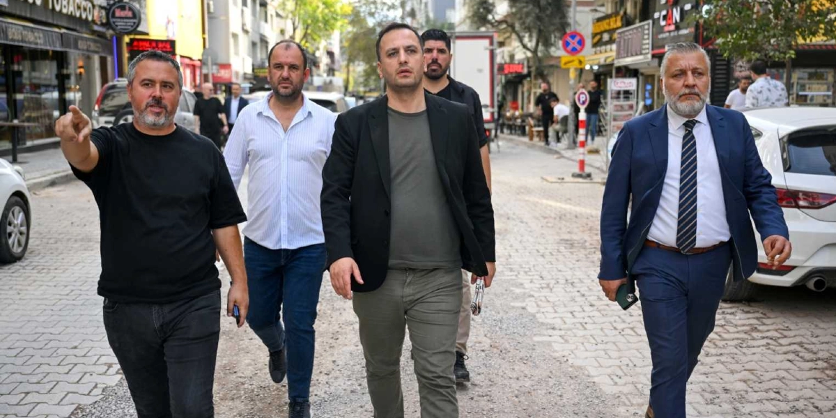 Süvari Caddesi'nde yürüyen dört kişilik bir grup, yenileme çalışmalarının yapıldığı caddede incelemelerde bulunuyor. En önde siyah tişörtlü bir adam eliyle bir noktayı işaret ederken, yanında beyaz gömlekli, siyah ceketli ve lacivert takım elbiseli üç adam ona eşlik ediyor. Arka planda dükkanlar, park halindeki araçlar ve çalışma alanı görülüyor.