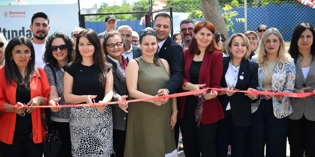 Bornova Belediyesi yetkilileri ve kadınların, bir tesisin açılışını yapmak üzere ellerinde makaslarla yan yana dizilerek kırmızı kurdeleyi kestikleri an.