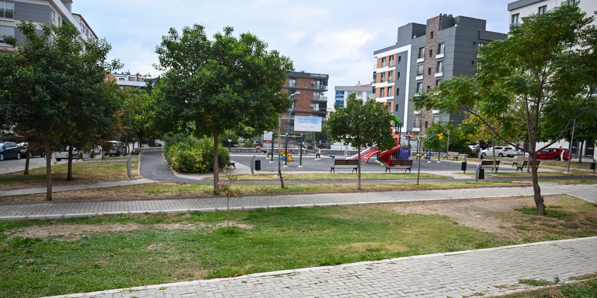 Bornova'da çok katlı modern apartmanların çevrelediği, ağaçlarla çevrili bir park alanı. Parkın orta kısmında çocuk oyun grubu, banklar ve yürüyüş yolları bulunuyor. Arka planda yer alan bir binanın üzerinde 