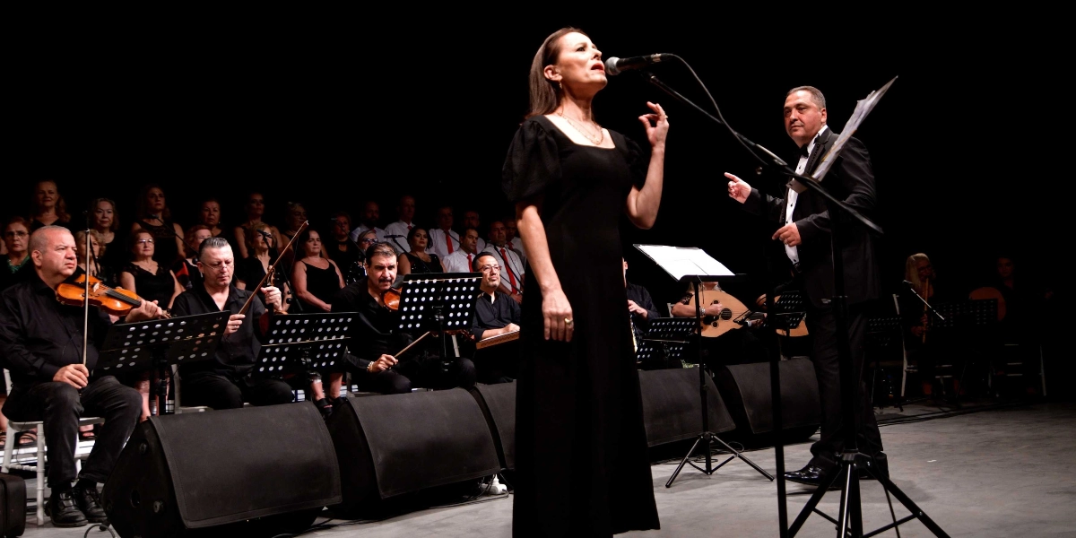 Siyah bir sahnede, uzun siyah bir elbise giymiş kadın solist mikrofon başında şarkı söylüyor. Solistin hemen sağında, siyah takım elbiseli bir orkestra şefi el hareketleriyle grubu yönetiyor. Arka planda ise keman, ud ve diğer enstrümanları çalan müzisyenlerden oluşan bir orkestra ve koro yer alıyor. Müzisyenlerin tamamı siyah kıyafetler içinde ve önlerinde nota sehpaları bulunuyor.