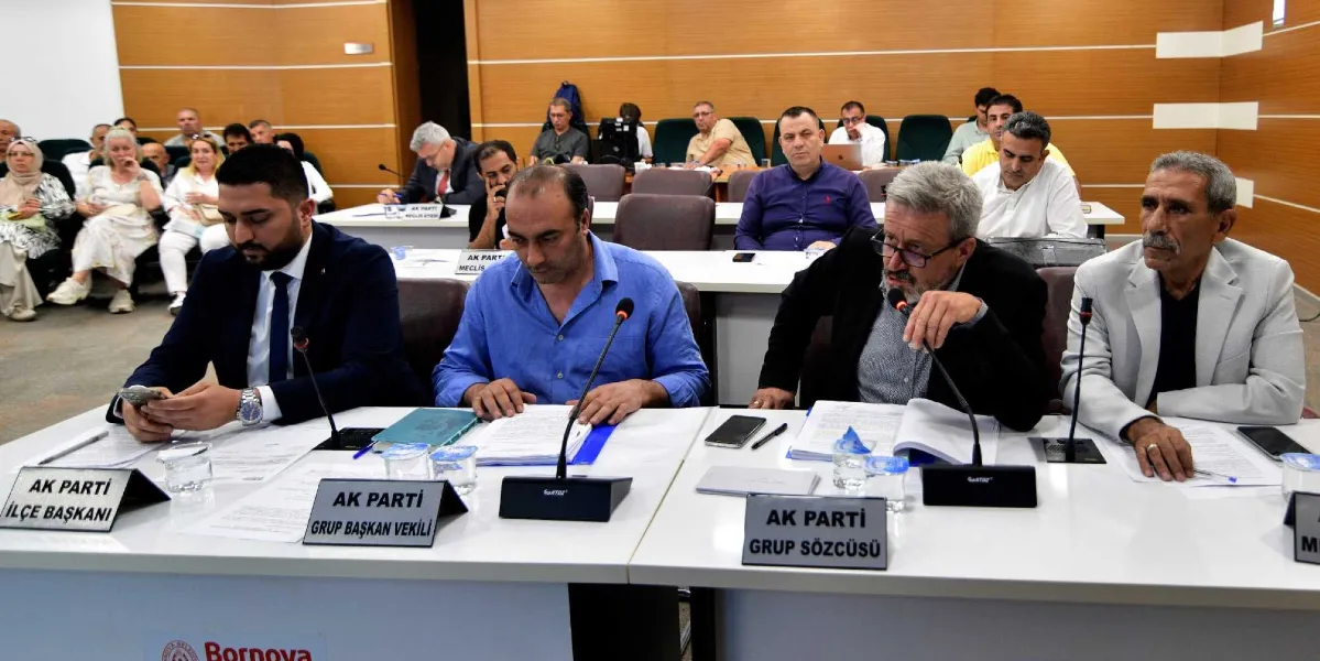 Bornova Belediyesi meclis salonunda düzenlenen toplantıda, ön masada oturan dört kişi yer alıyor. Masanın üzerinde 